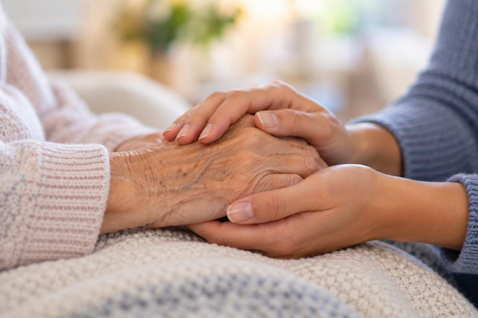 A carer gently holding the hands of an elderly client, offering comfort and companionship